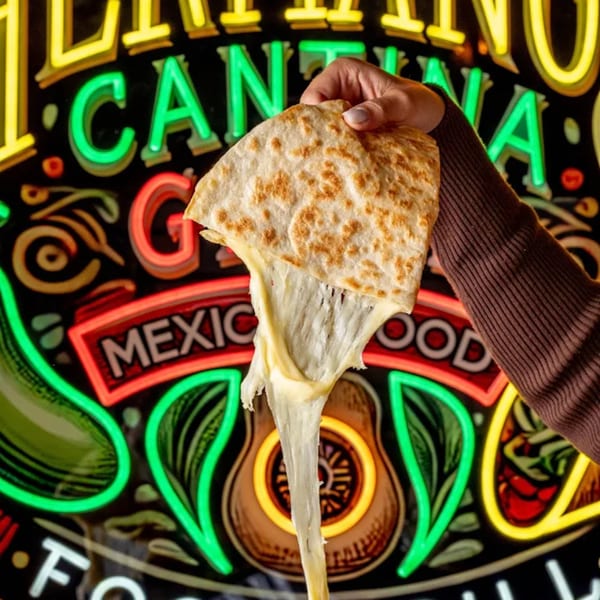 Hand holding a cheesy quesadilla with melted cheese stretching against a neon sign background.