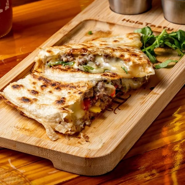 Grilled quesadillas filled with melted cheese, ground meat, and vegetables on a wooden board.