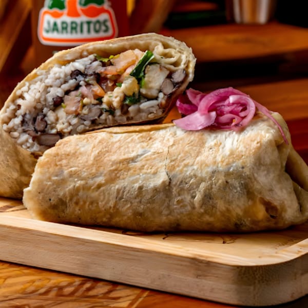 A sliced Hermanos Cantina Grill burrito with rice, beans, and meat, topped with pickled onions.