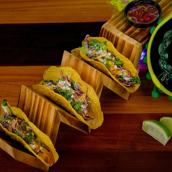 Three Hermanos Cantina Grill tacos in wooden holders, with salsa, lime, and a sombrero.